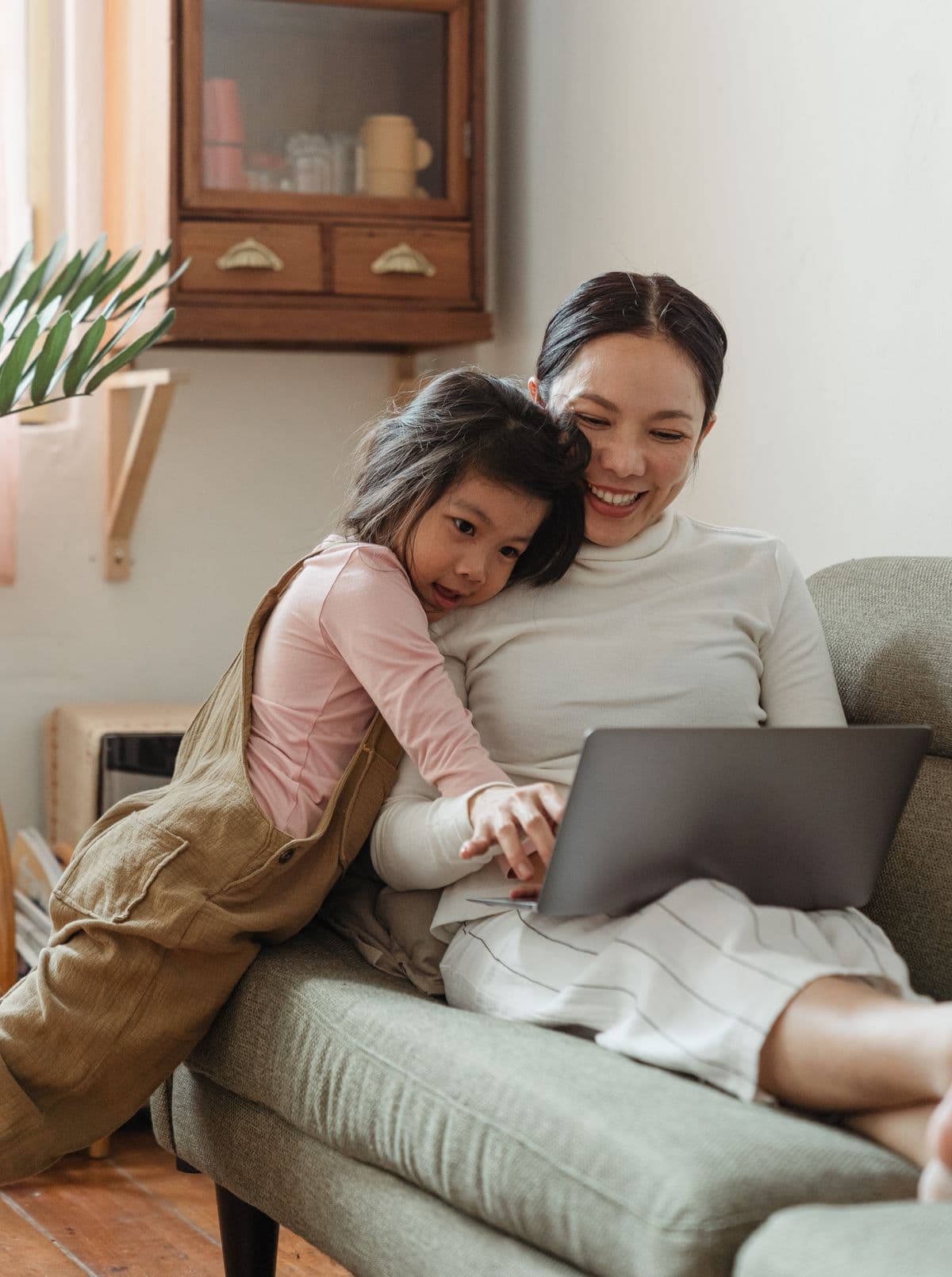 A smiling parent and child cuddled together on a sofa, looking at a laptop together